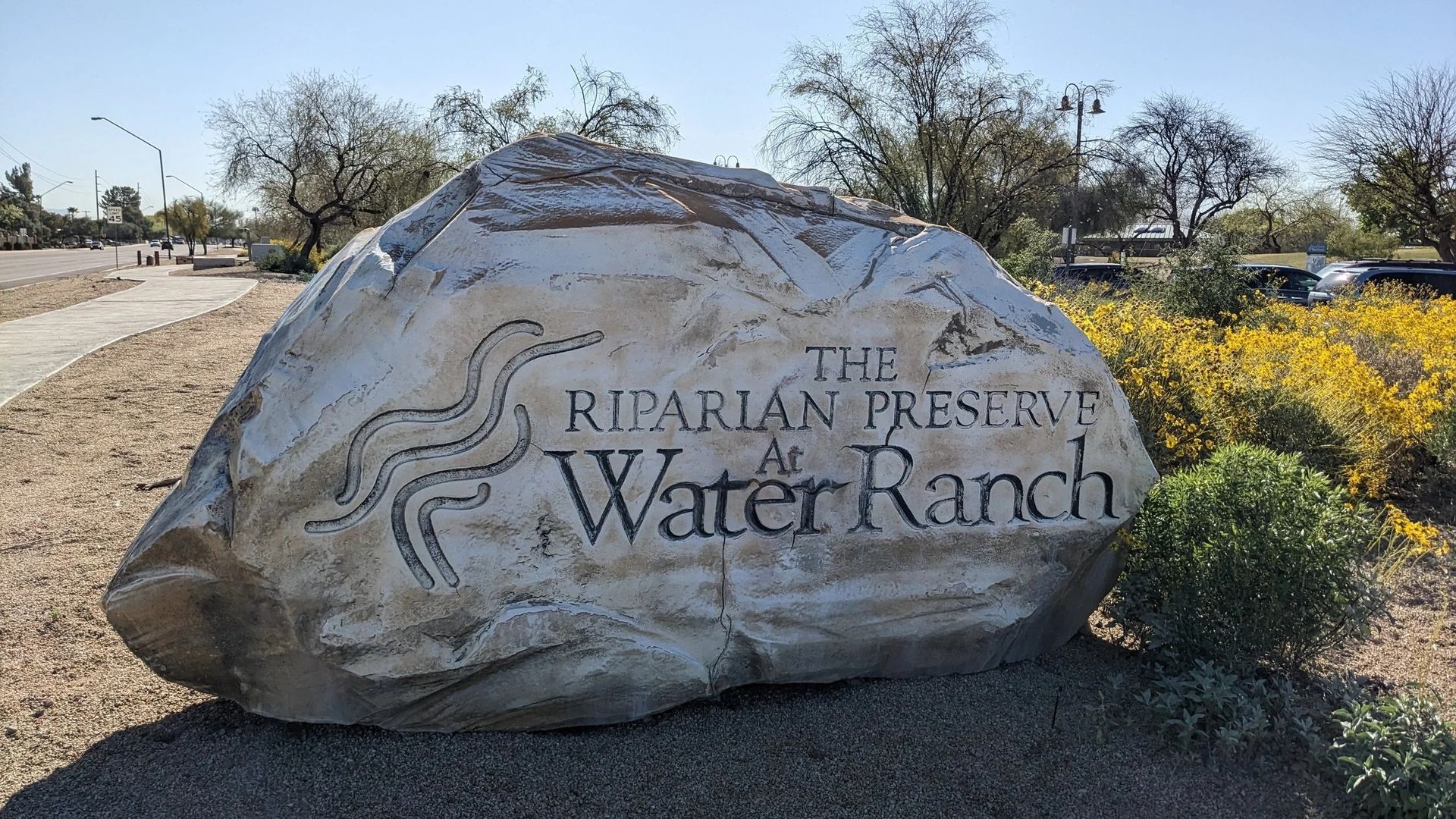 Large stone sign for the Riparian Preserve at Water Ranch. White rock with black text, winding river graphic.