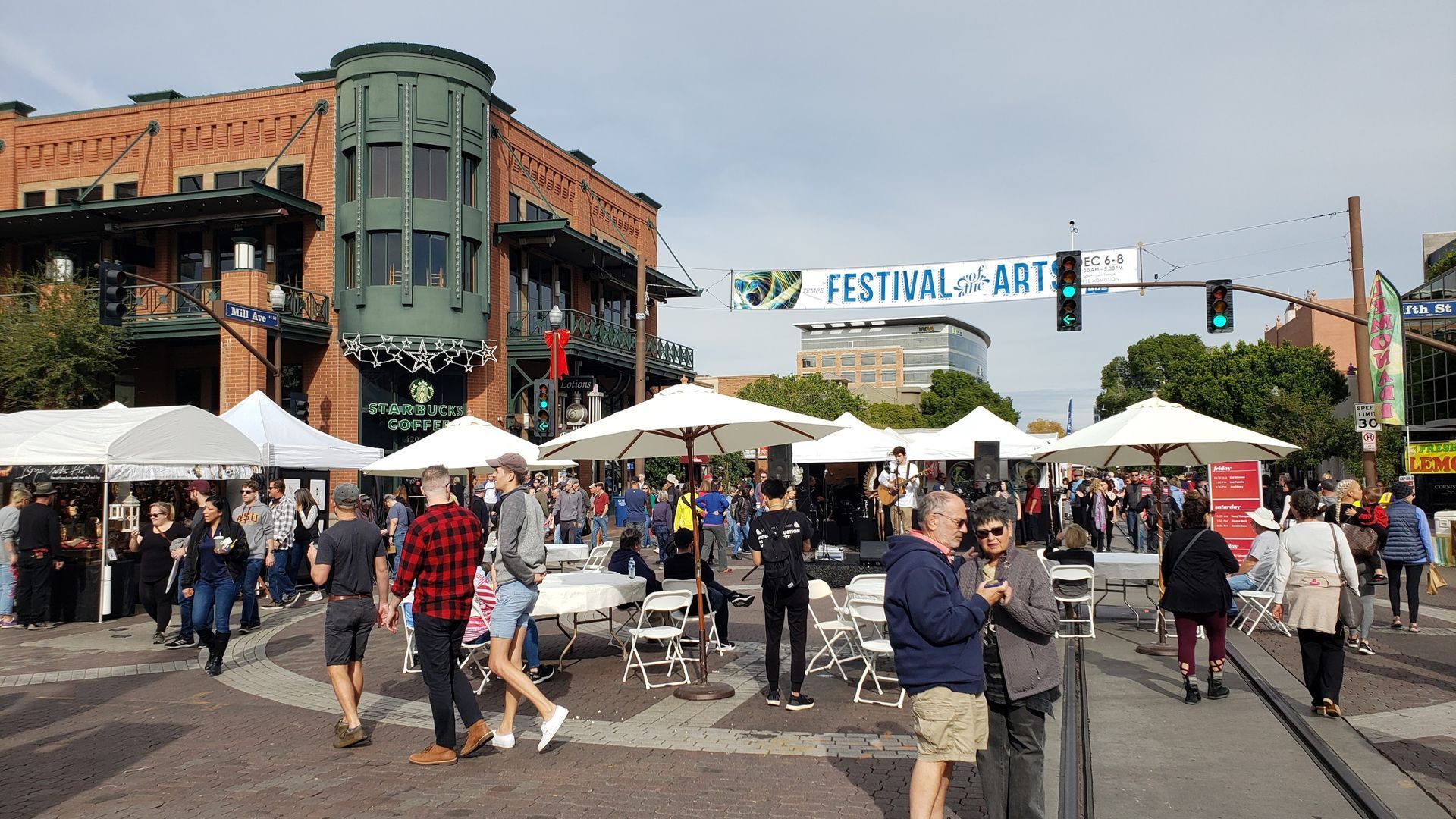 Festival of Arts on a city street. Crowds of people walking around white tents and tables. Buildings in the background.