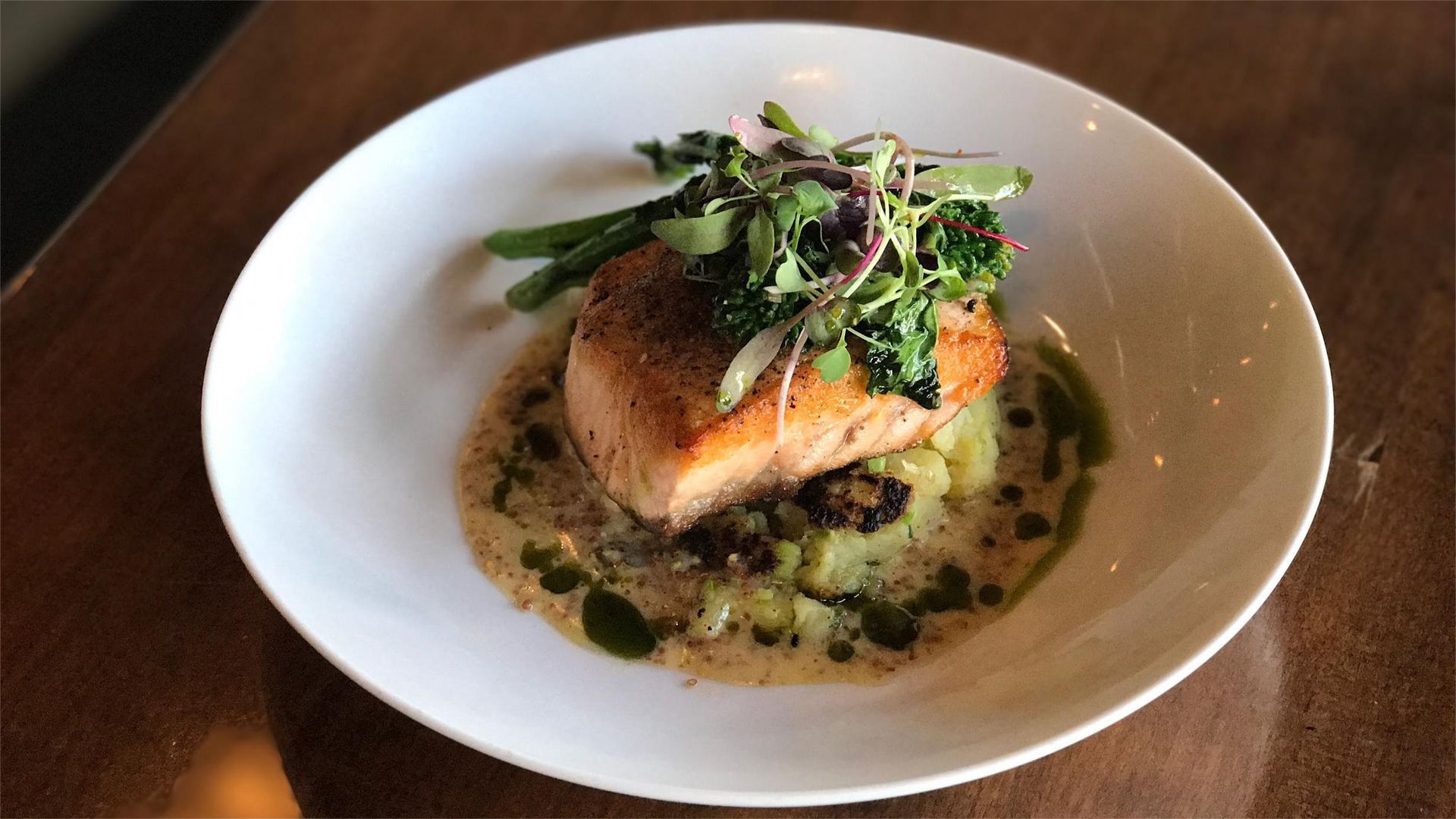 Salmon fillet with greens, green beans, and sauce in a white bowl.