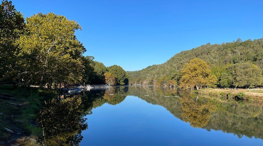 Calm river reflecting trees under a clear blue sky; forested hills in the background.