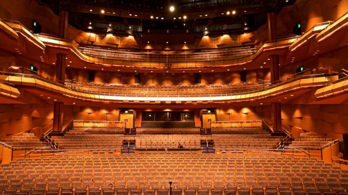 Empty, ornate theater with tiered seating and warm orange lighting.
