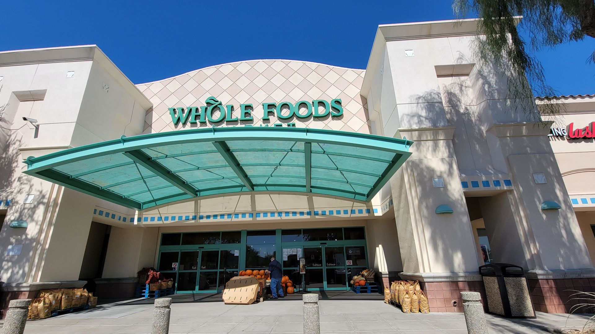 Whole Foods Market entrance with teal awning, under a clear blue sky.