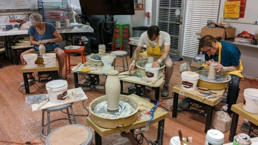 People working at pottery wheels in a brightly lit studio.