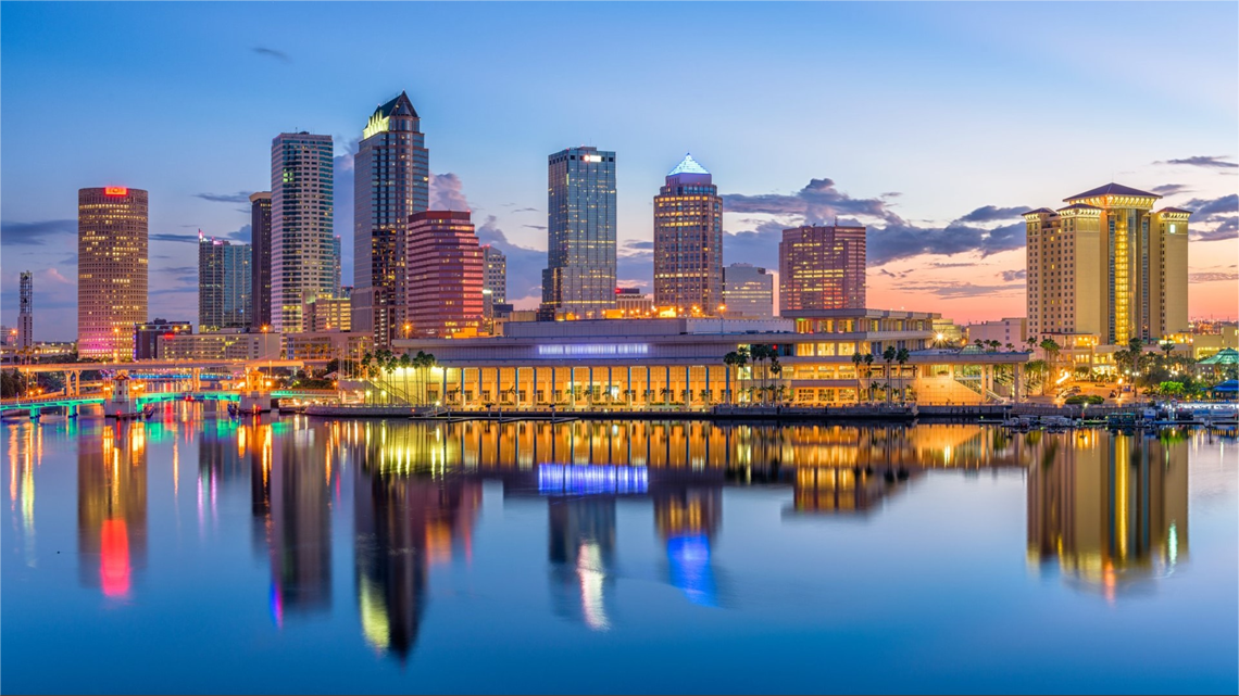 Tampa, Florida skyline reflecting in calm water at dusk with colorful lights.