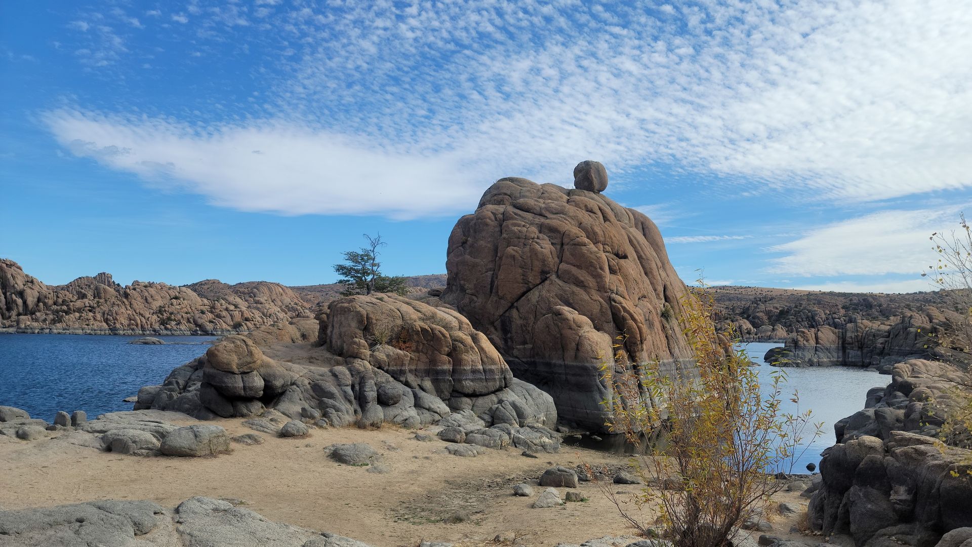 Rocky landscape with blue water and sky. Cloud-filled sky over large granite formations at Watson Lake.