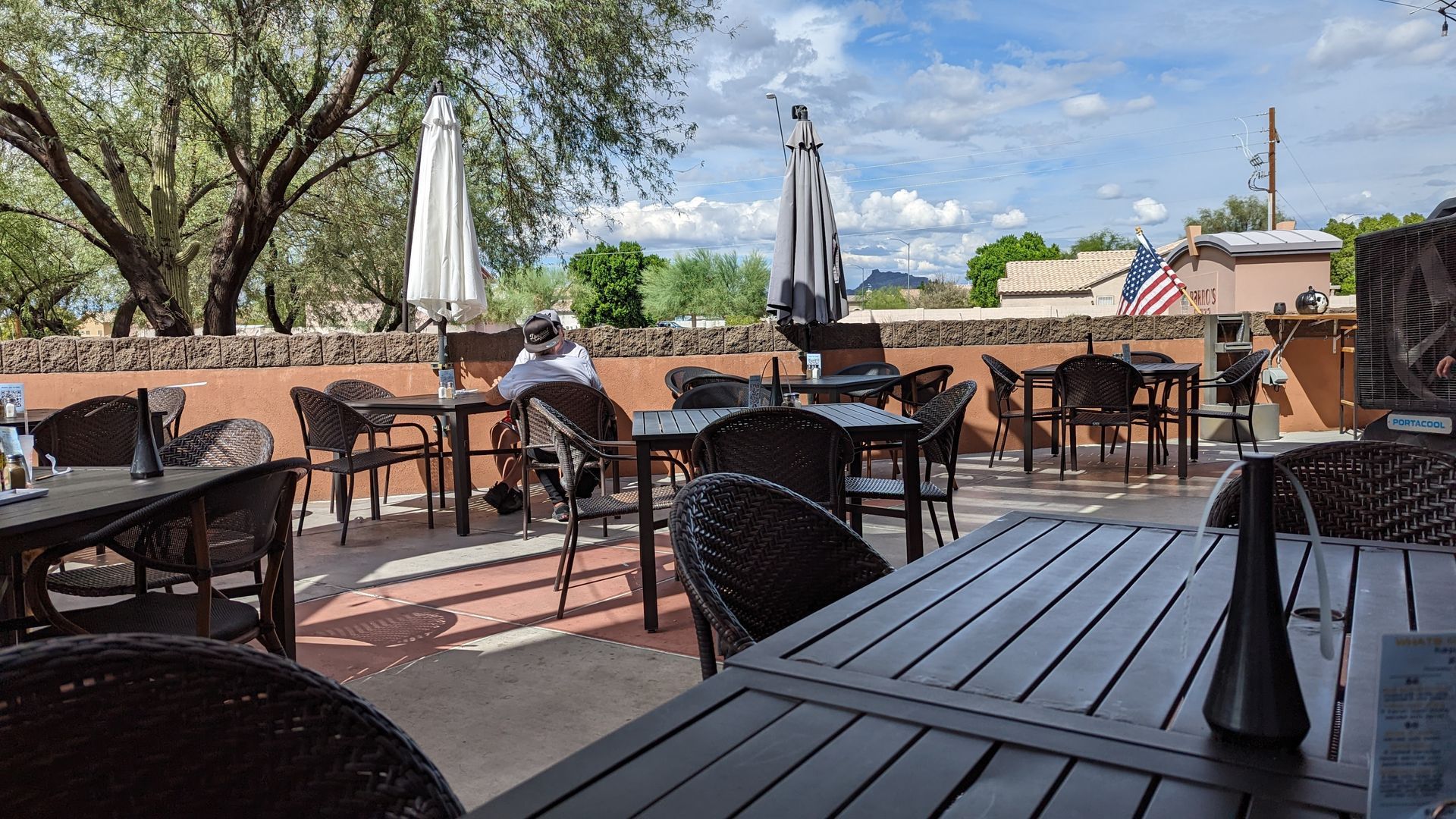 Outdoor restaurant patio with tables, chairs, and umbrellas under a cloudy sky.