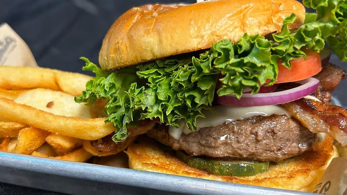 Burger with lettuce, tomato, red onion, bacon, and fries on a tray.