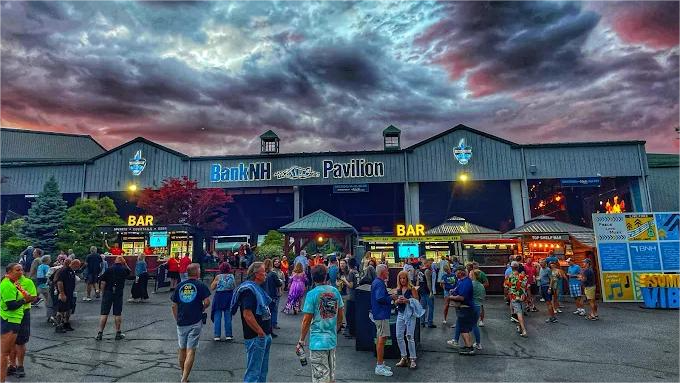 People gather at BankNH Pavilion under a stormy sky, enjoying outdoor food and drinks.