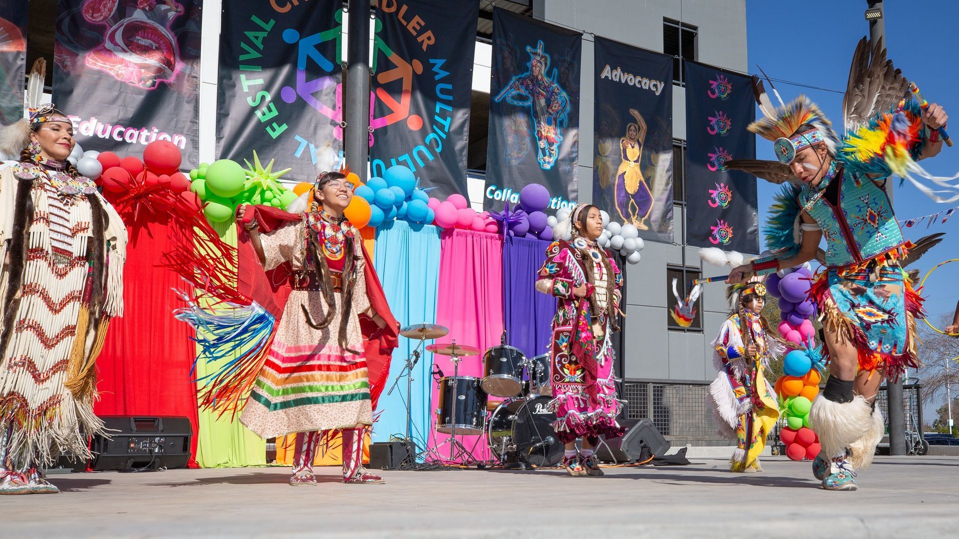 Native American dancers on stage with colorful balloons and banners, performing.