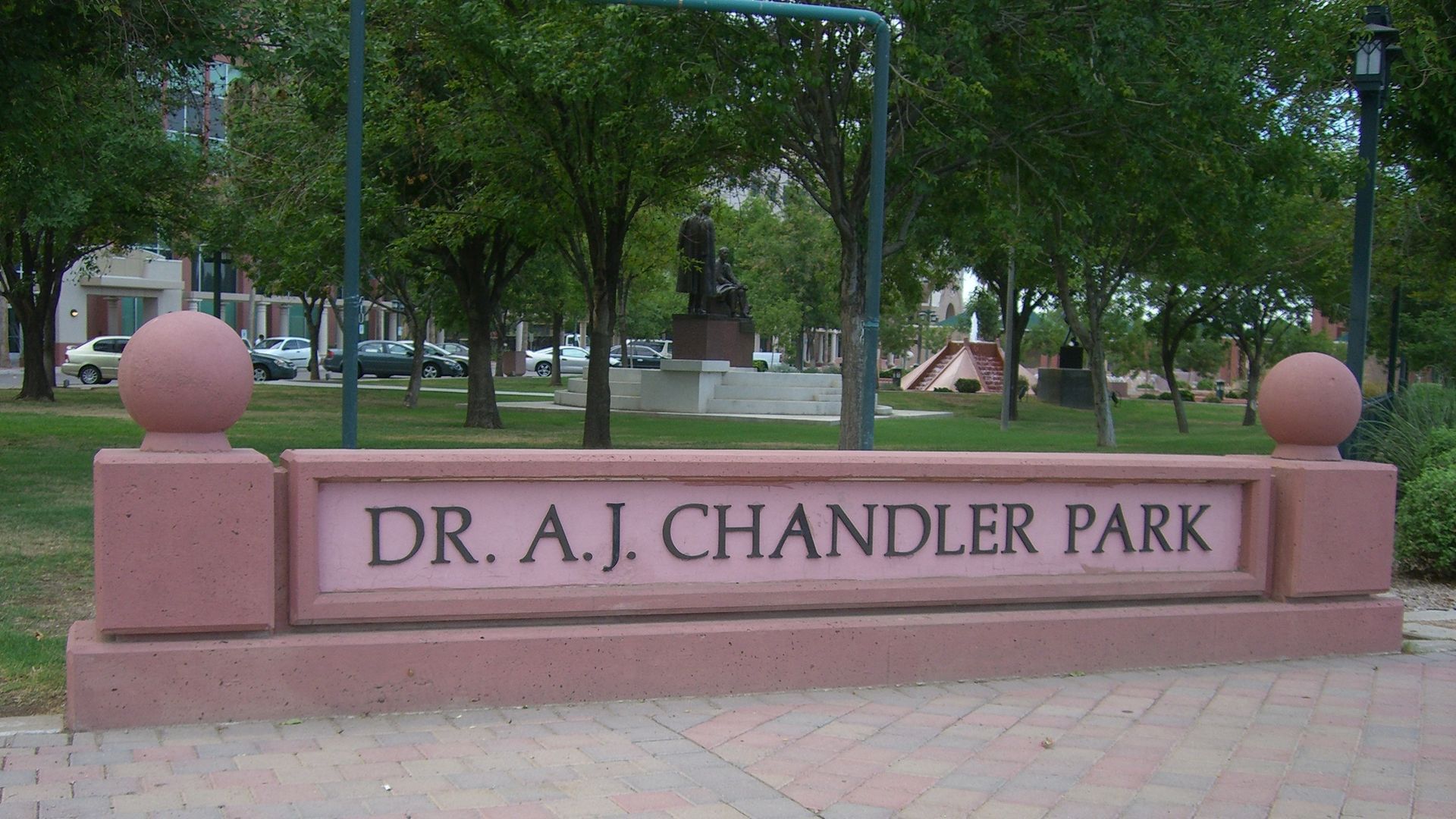 Sign for Dr. A.J. Chandler Park; pink concrete with engraved text, trees and green lawn in background.