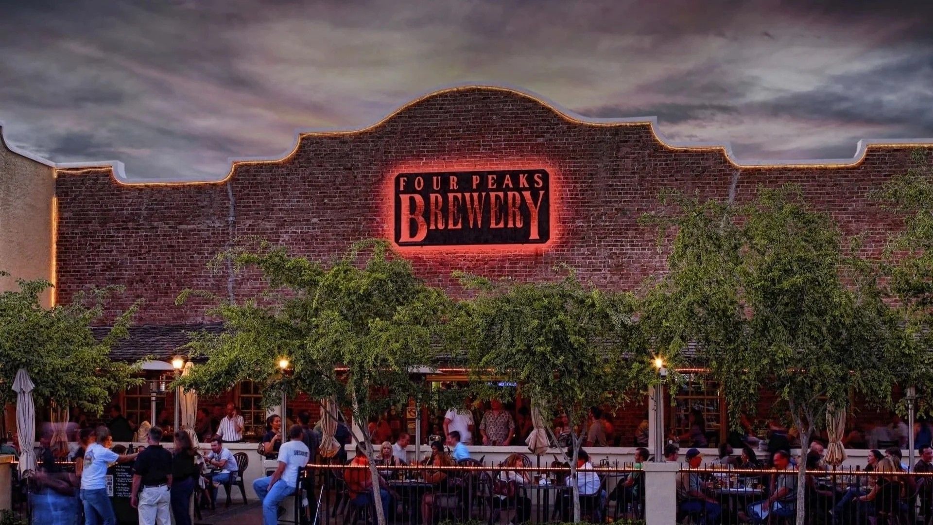 Exterior view of Firestone Walker Brewery at dusk, with patrons dining outdoors under trees.