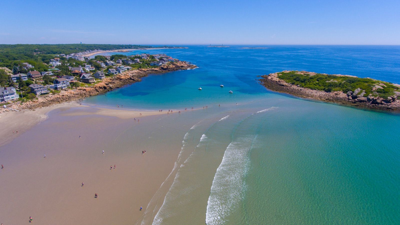 Aerial view of a beach with houses, ocean, and a small island on a sunny day.