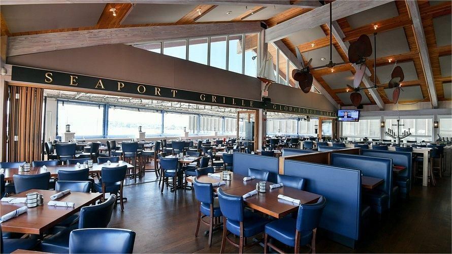 Interior of the Seaport Grille restaurant. Tables, blue chairs, booths, and large windows with water views.