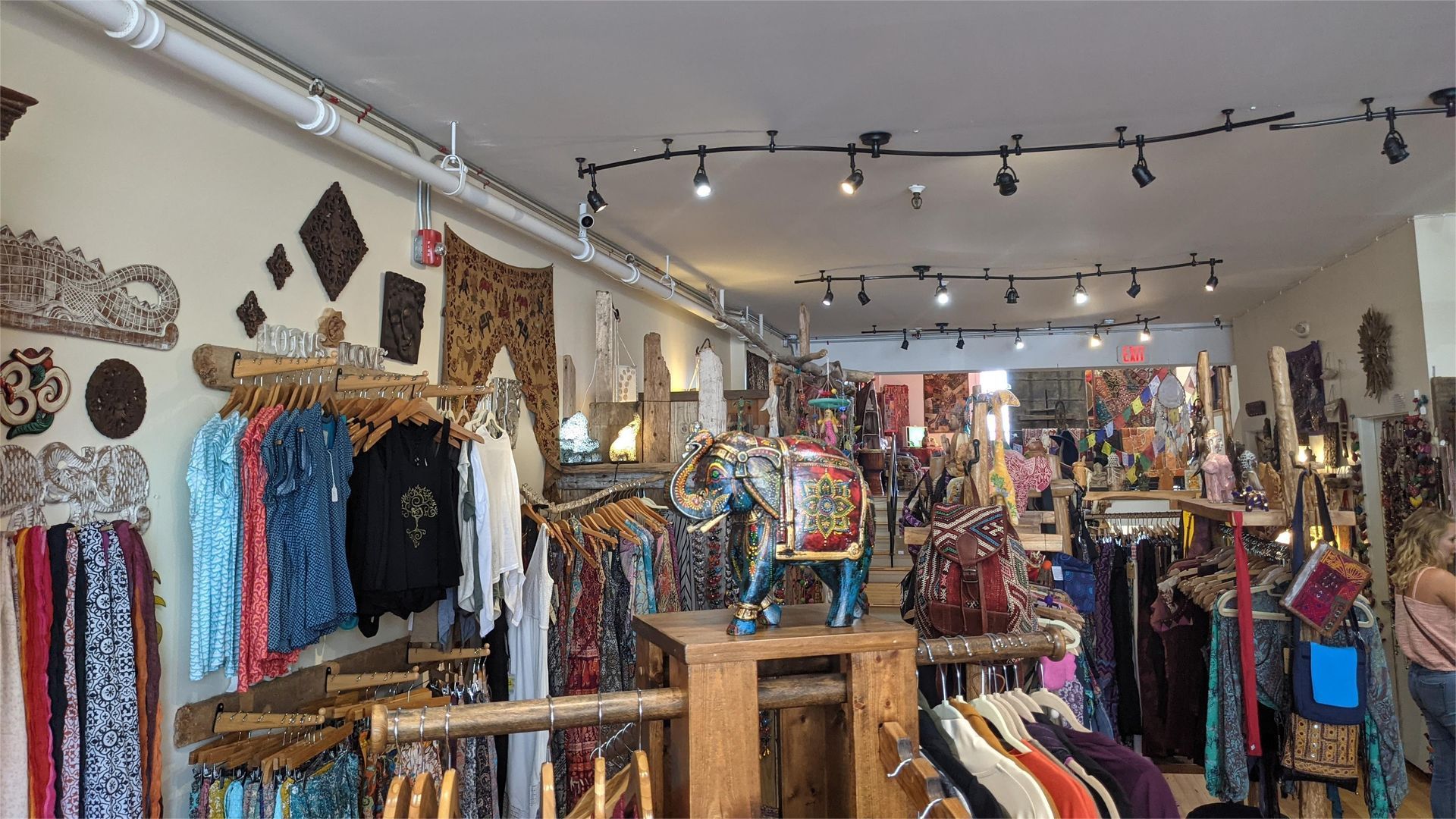 Inside a clothing and gift shop with racks of colorful apparel and decorative items on the walls.