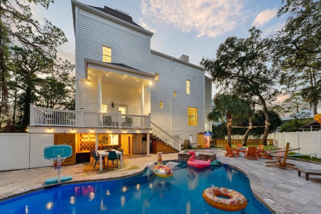 Backyard pool beside a white house at dusk, with colorful float rings and patio seating
