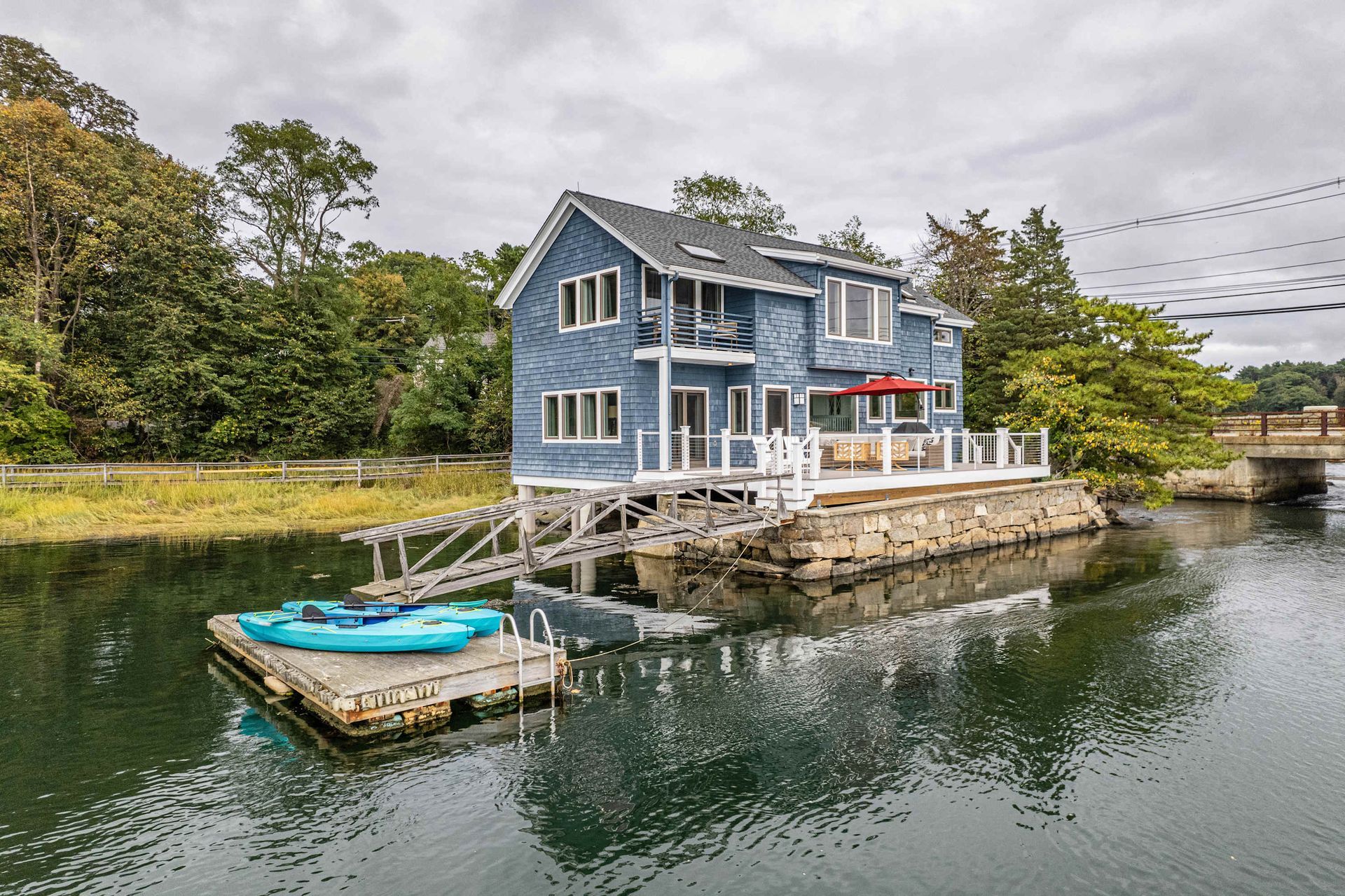 Blue waterfront house with dock and small boat on calm canal, surrounded by trees