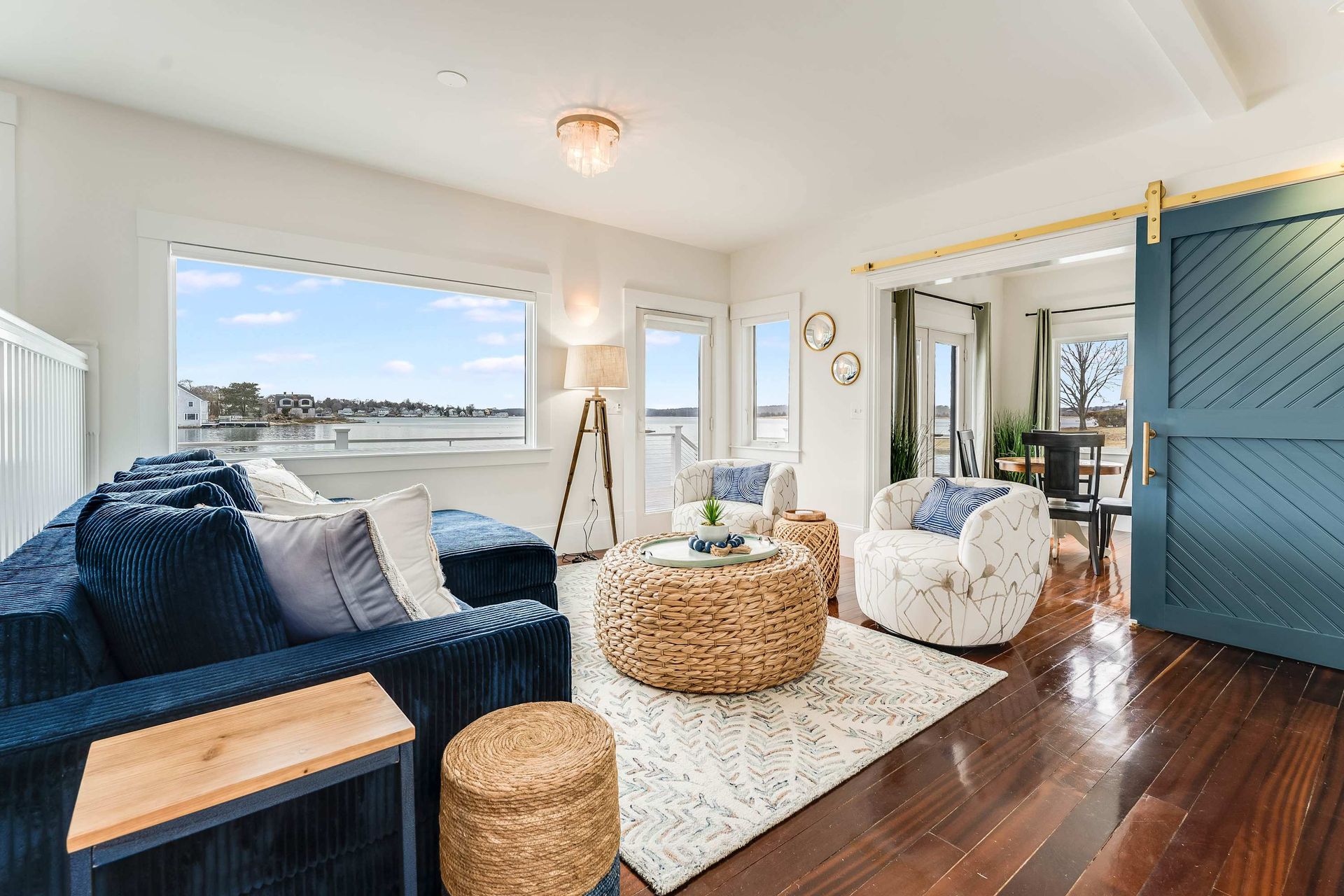 Bright living room with blue sofa, woven chairs, large window, and ocean view