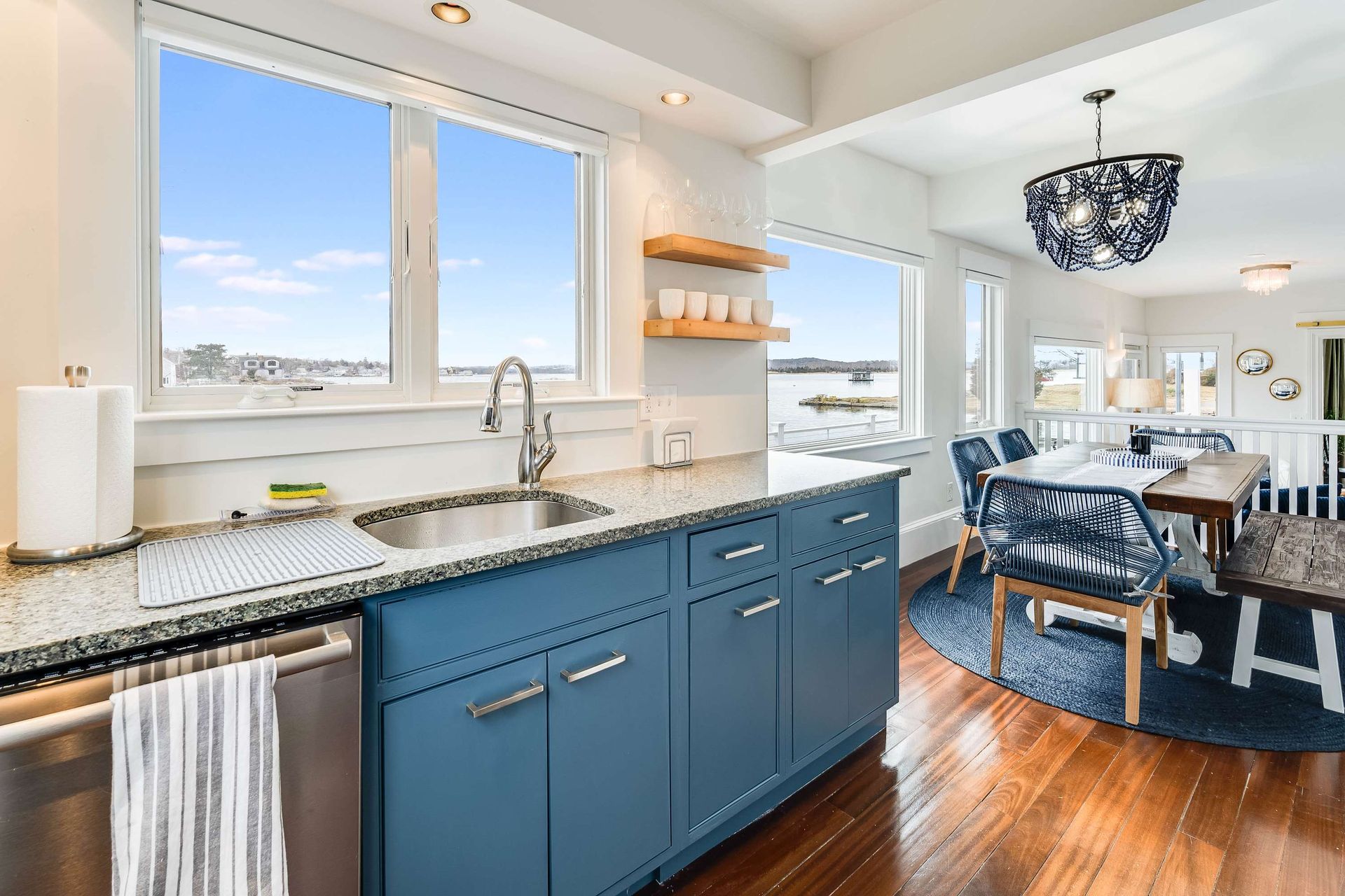 Bright modern kitchen with blue cabinets, granite countertop, and dining area overlooking water.