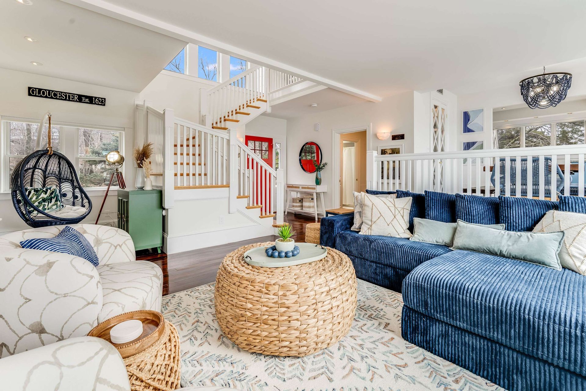 Bright coastal living room with blue sofa, wicker coffee table, white stairs, and patterned rug