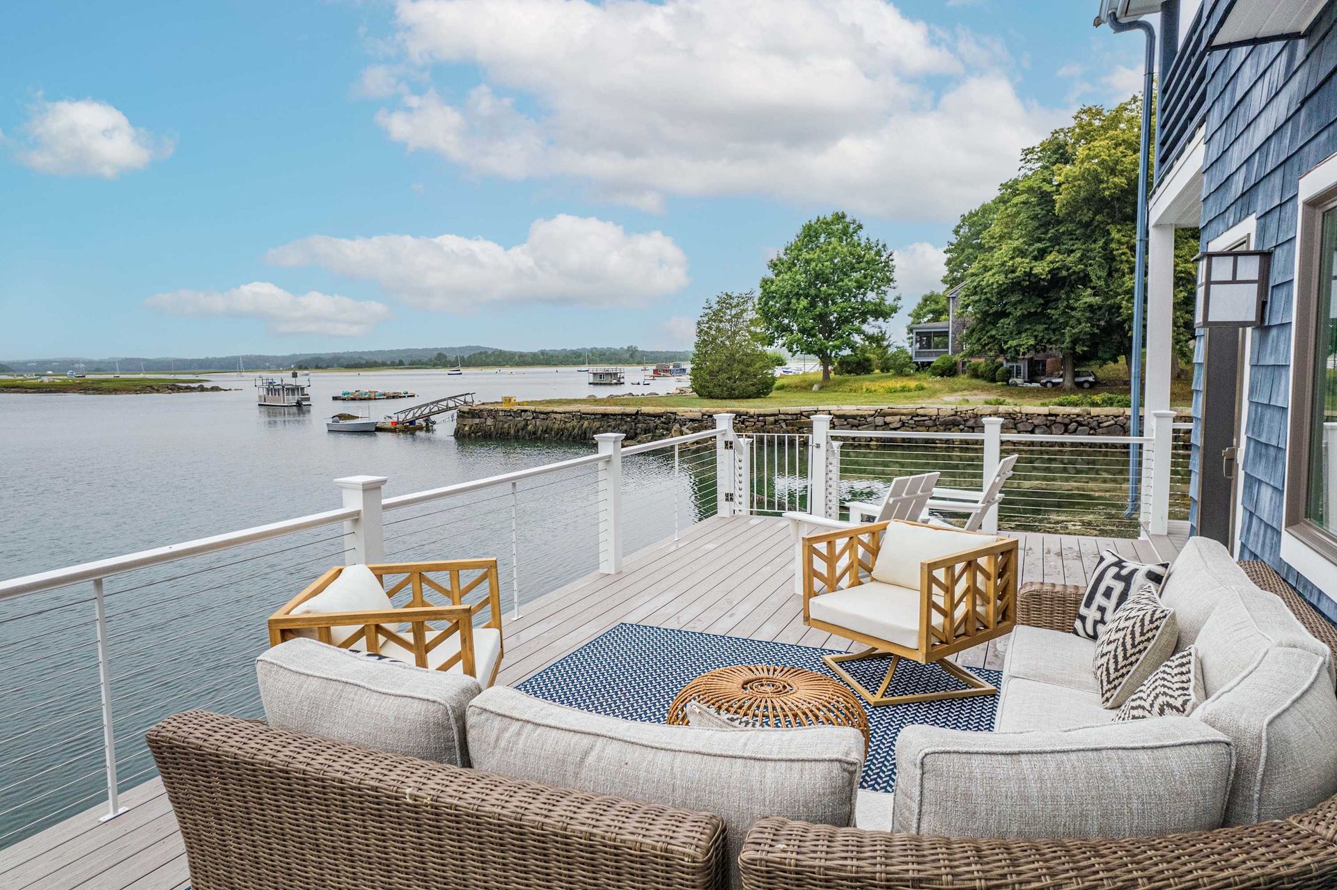 Waterfront deck with wicker seating, striped cushions, and a view of the bay and boats