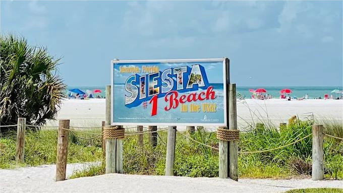 Sign for Siesta Key Beach on sandy path with beachgoers in the distance.