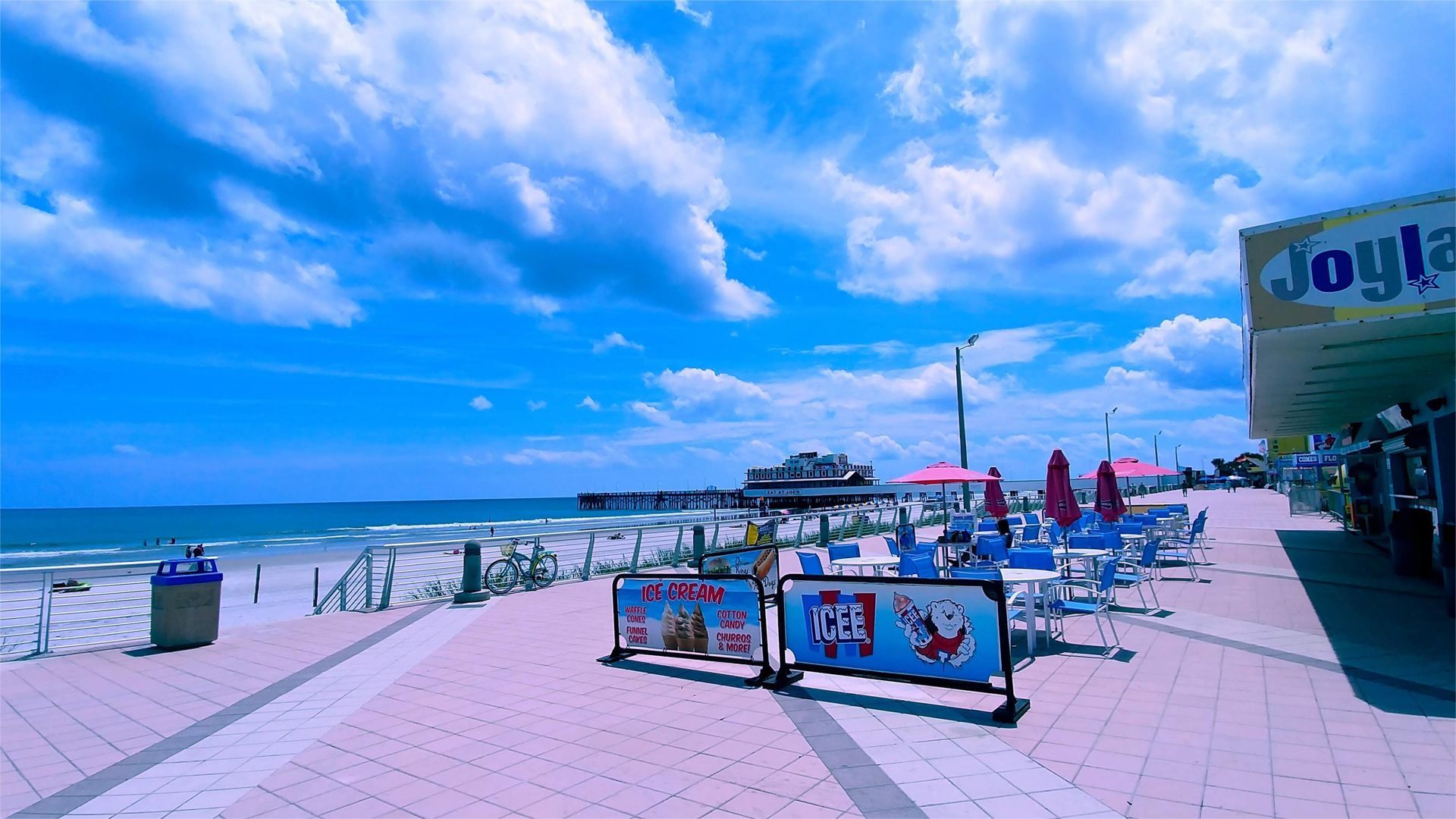 Beachfront boardwalk scene under a bright blue sky with fluffy clouds. Joyland amusement park sign visible.