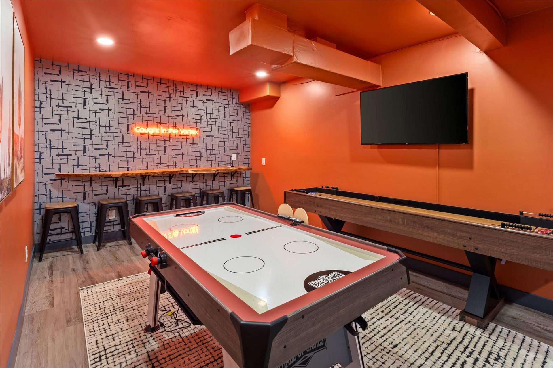 Orange game room with air hockey table, pool table, stools, wall art, and a mounted TV