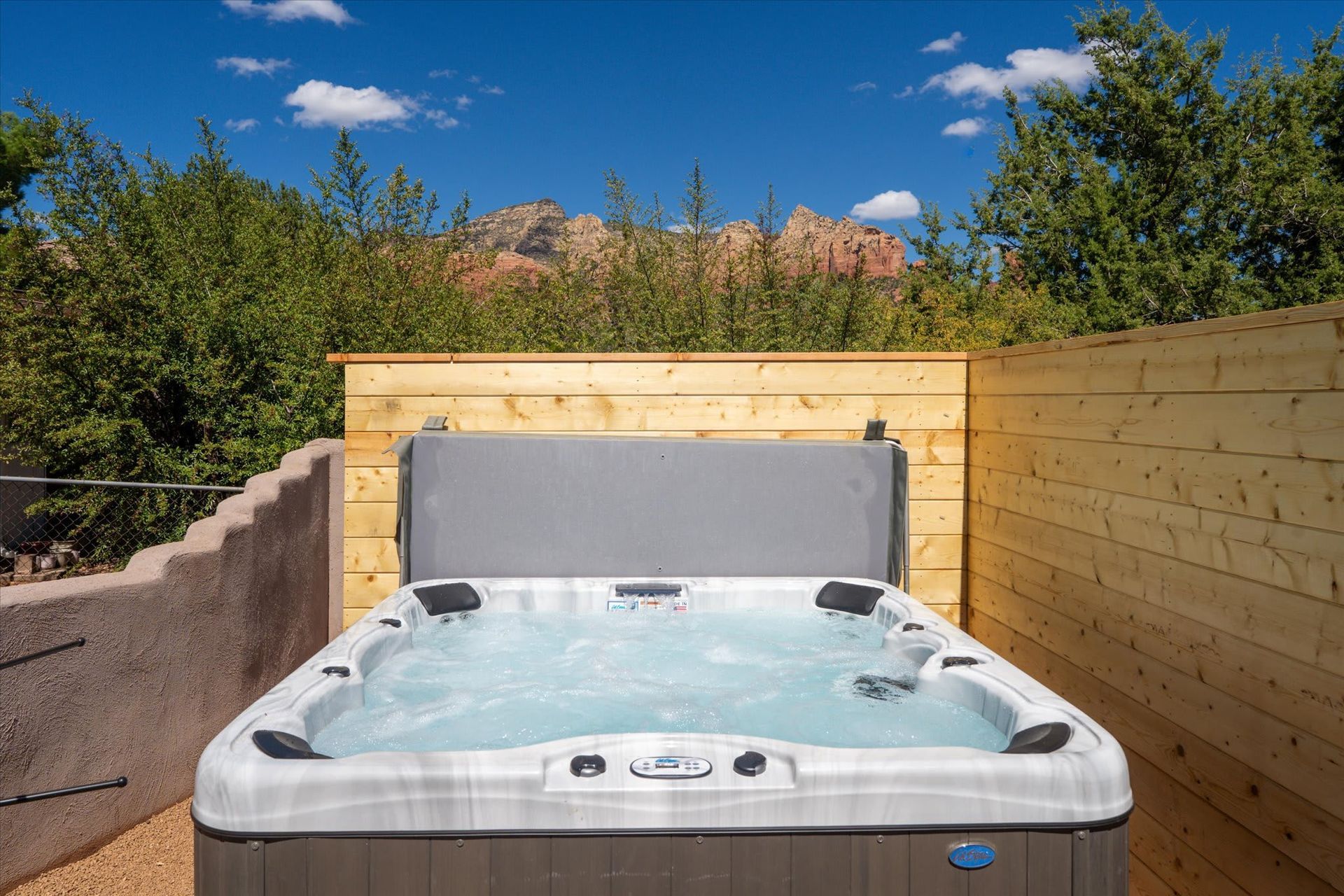 Outdoor hot tub in a fenced backyard with mountains and blue sky in the background