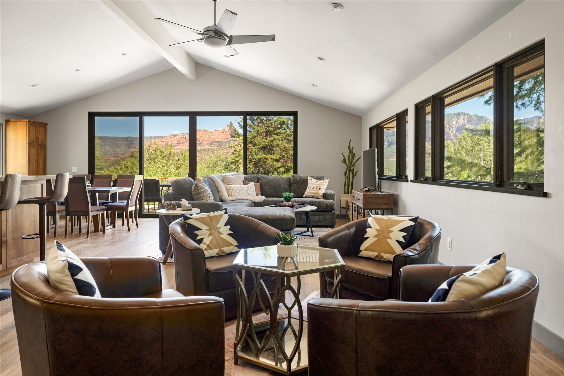 Bright open living room with leather chairs, sofa, dining area, and large windows overlooking a scenic view