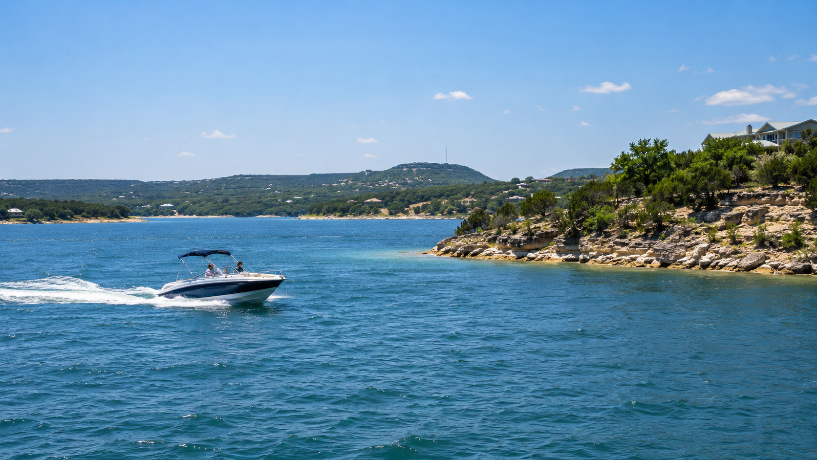 Motorboat speeding across blue water near a rocky, tree-lined shoreline under a clear sky