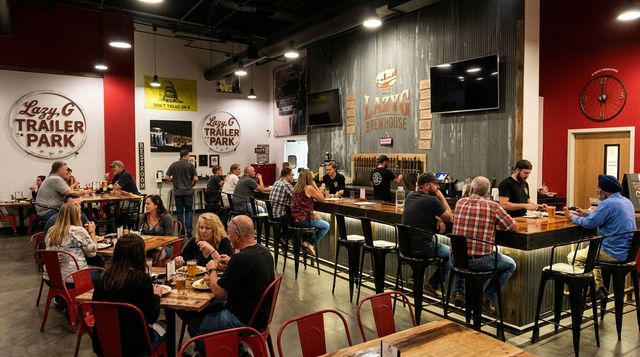 Bustling brewery taproom with people seated at tables, warm lighting, and a wall-mounted TV