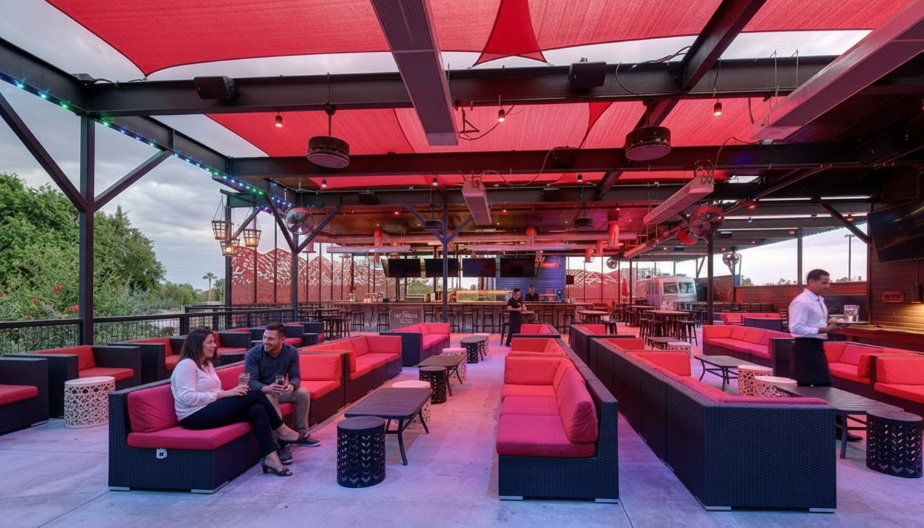 Open-air lounge with red-lit seating, people relaxing, and a bar under a metal canopy with city views