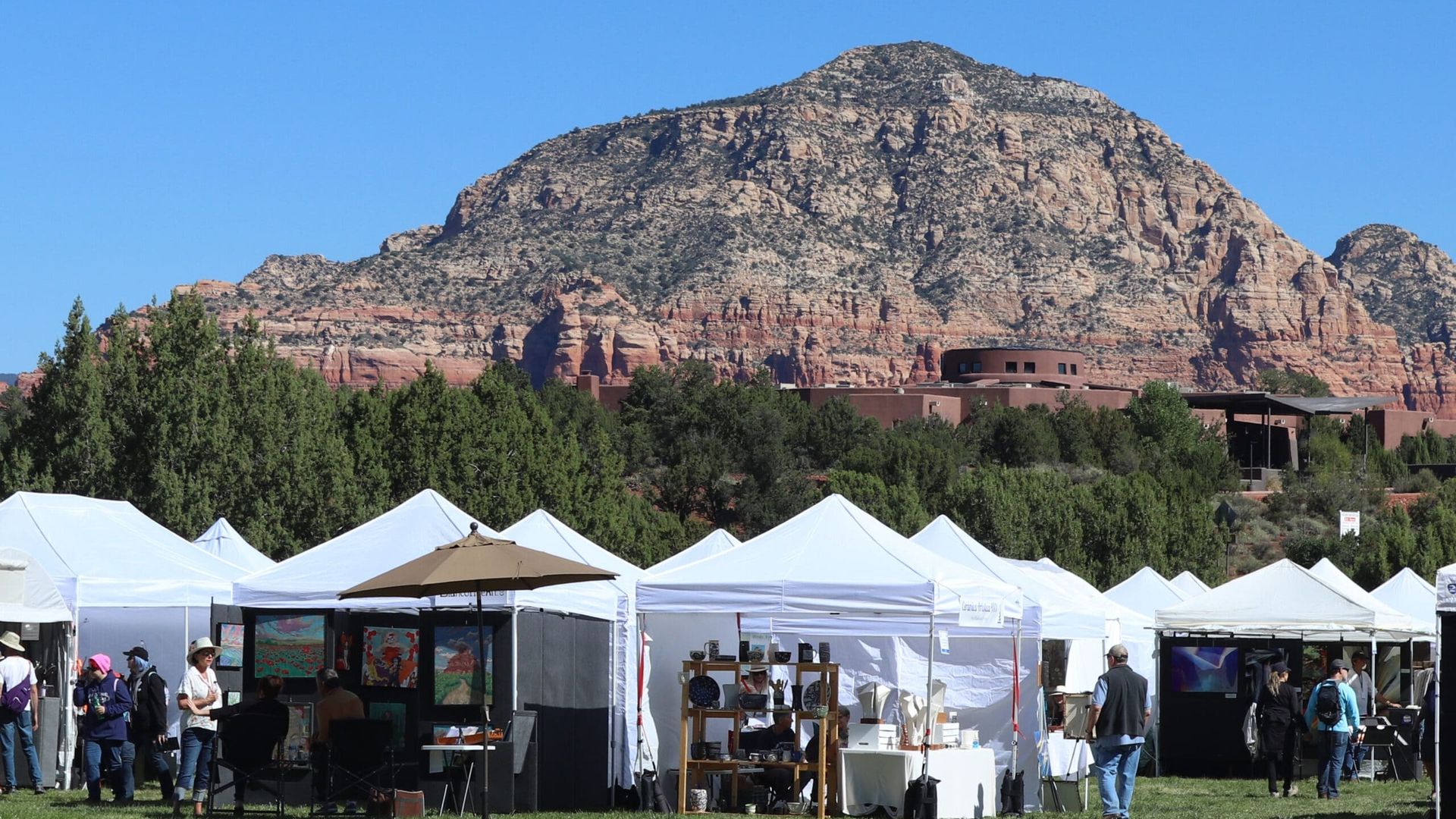 Art fair with white tents in a field, red rock mountain background.
