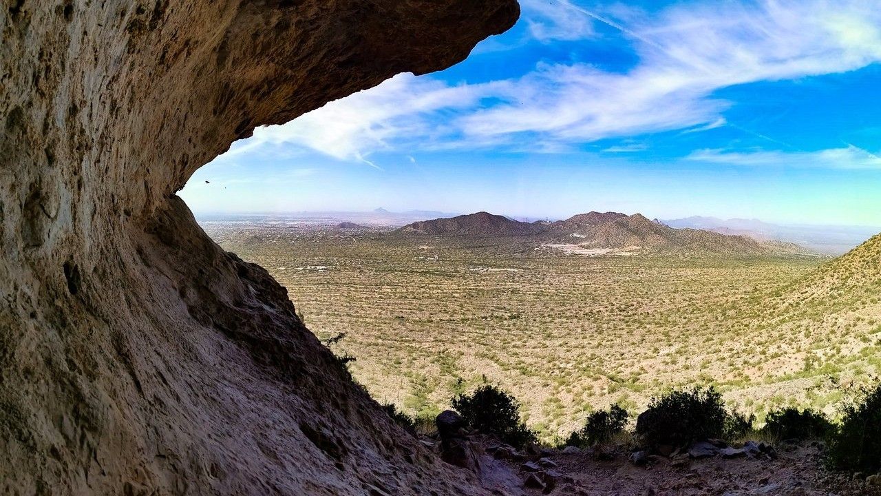 View from a cave opening overlooking a desert landscape under a blue sky.
