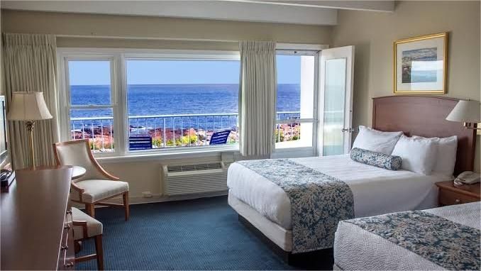 Hotel room with two beds, a large window overlooking the ocean. Light blue and white decor.