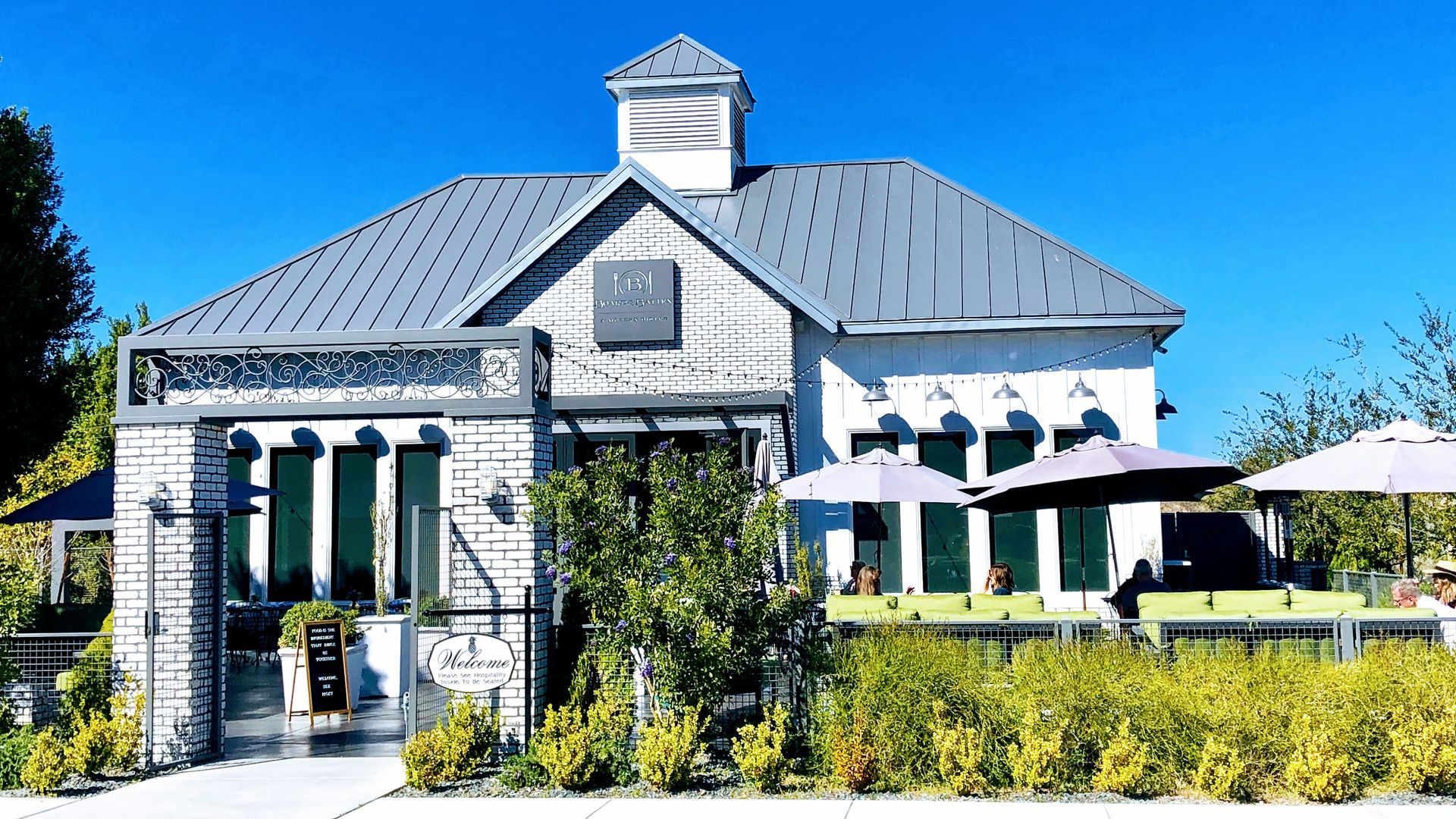 White building with gray roof and outdoor seating under blue sky.