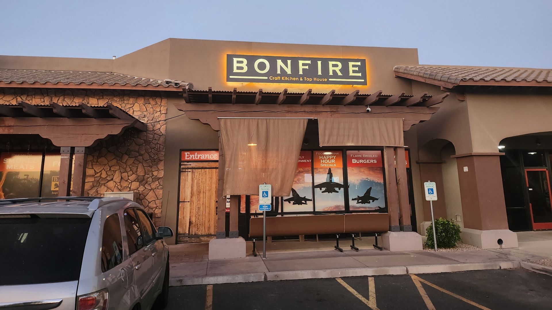 Bonfire Restaurant exterior with illuminated sign. Beige building with outdoor seating and parking.