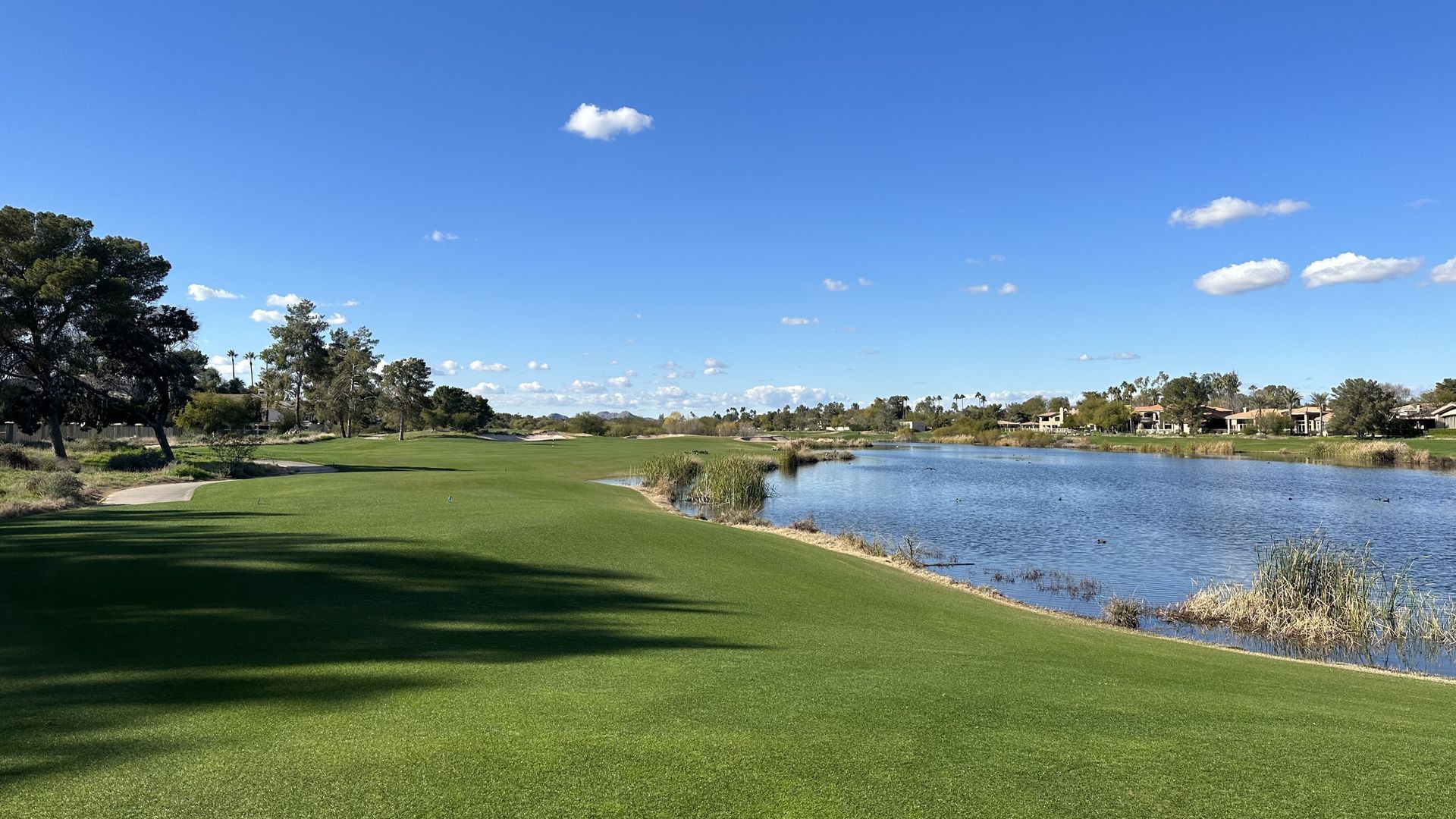 Green golf course with a lake and blue sky.