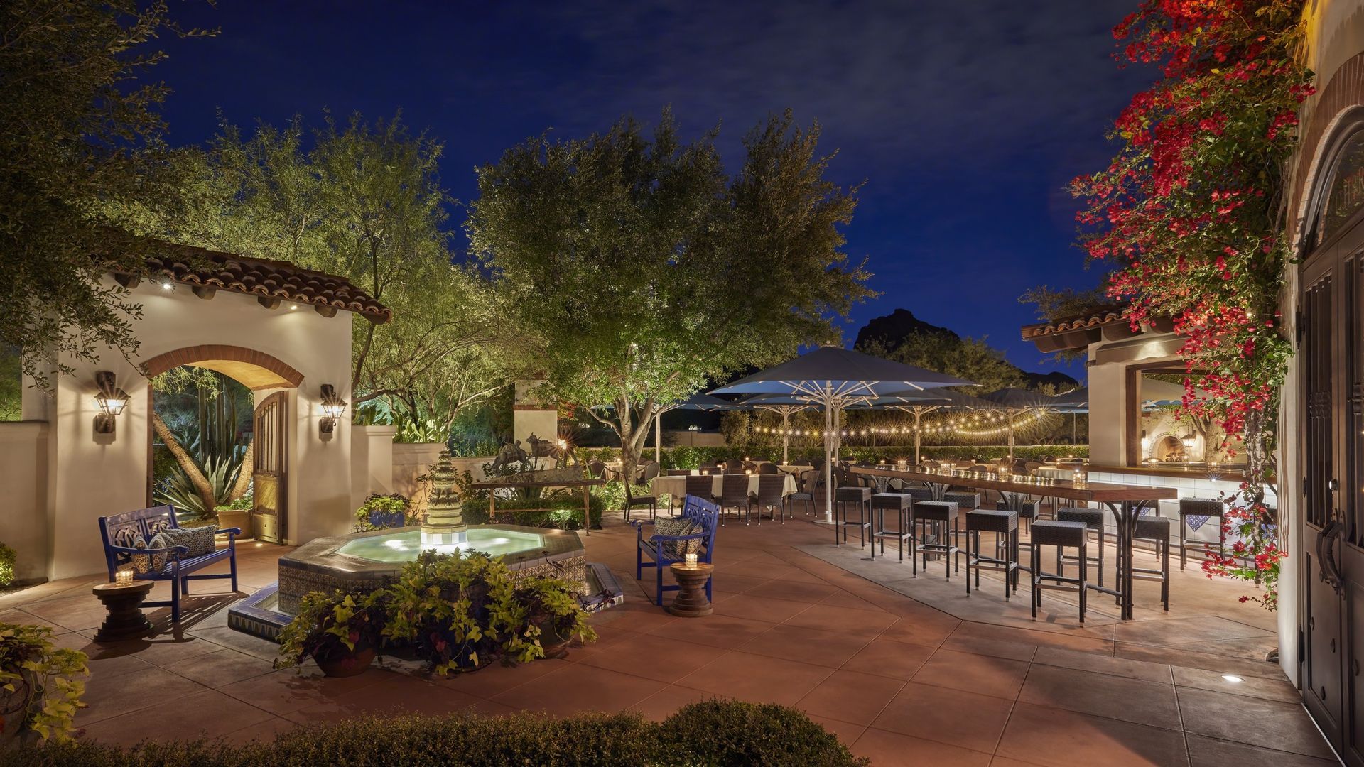 Outdoor evening restaurant patio with tables, fountain, and string lights.