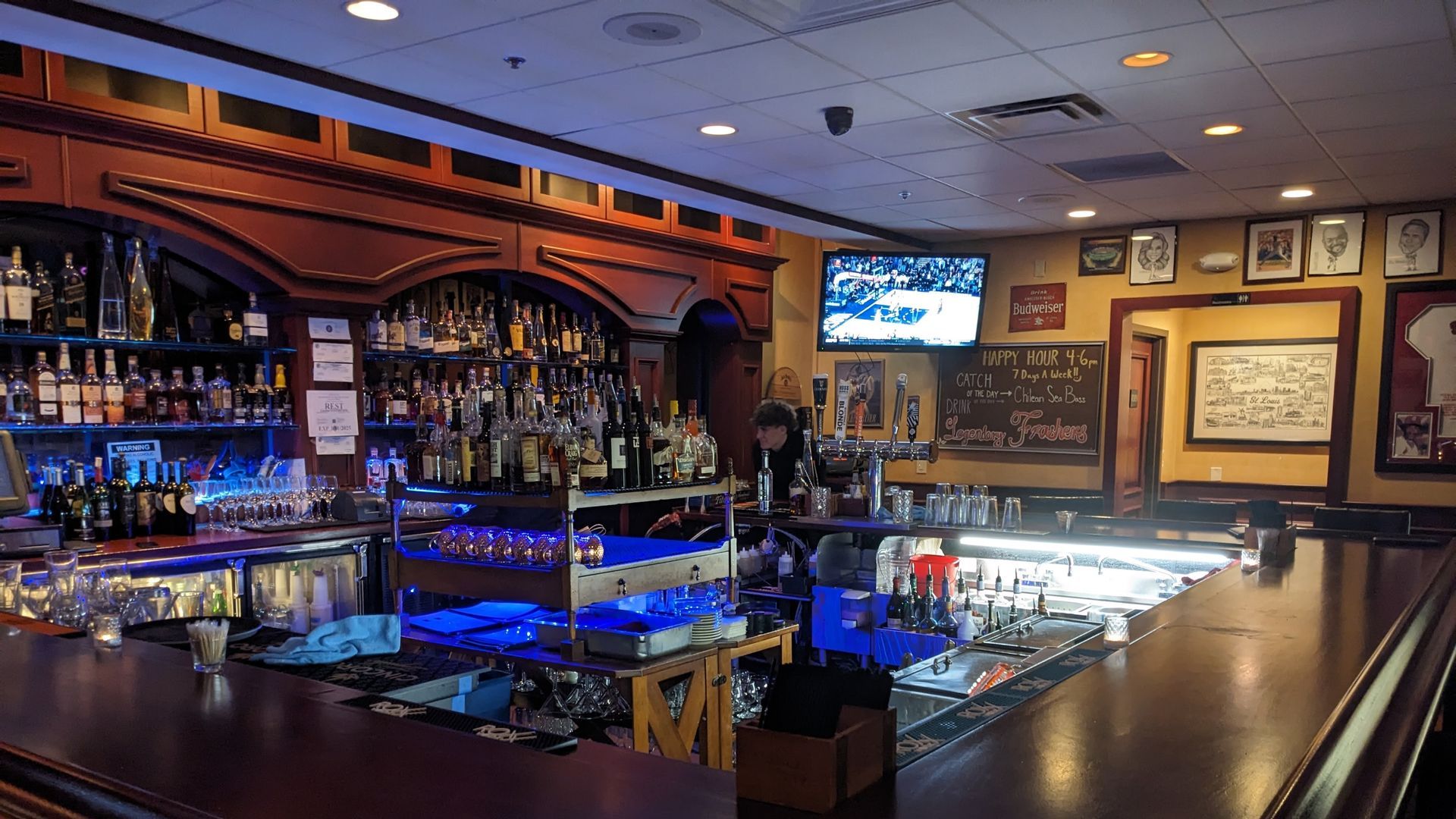 Bar interior with bottles of liquor, a TV showing sports, and barstools.