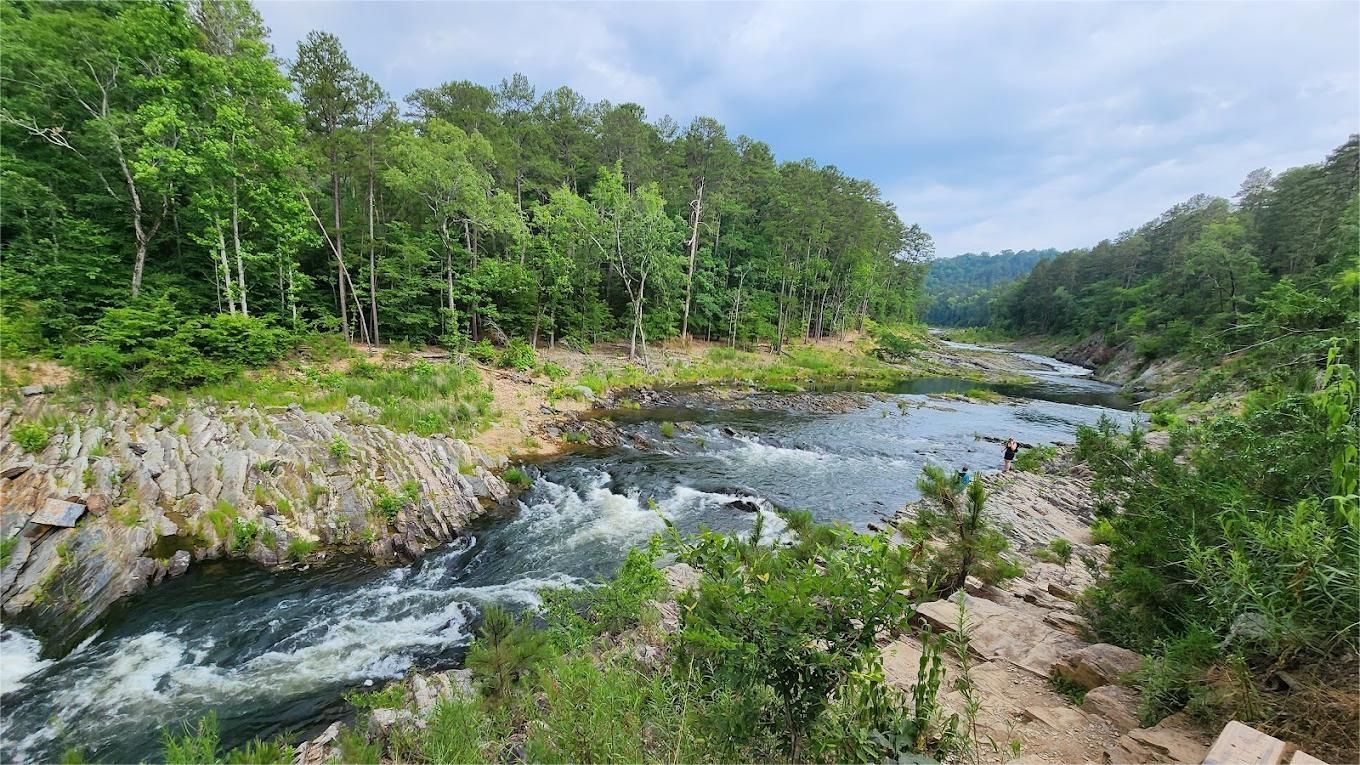 River flowing through a rocky gorge, surrounded by lush green trees under a cloudy sky.