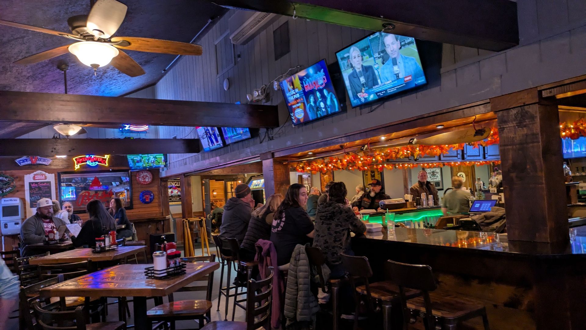 Bar interior with patrons seated at tables and bar, multiple TVs, bartender serving drinks.