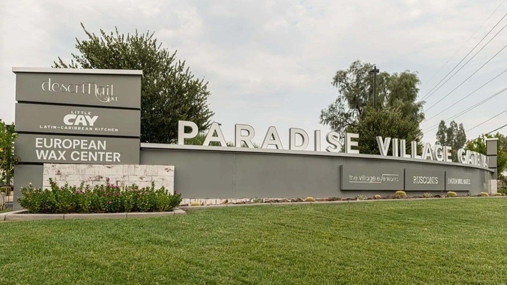 Sign for Paradise Village Center with business names and foliage.