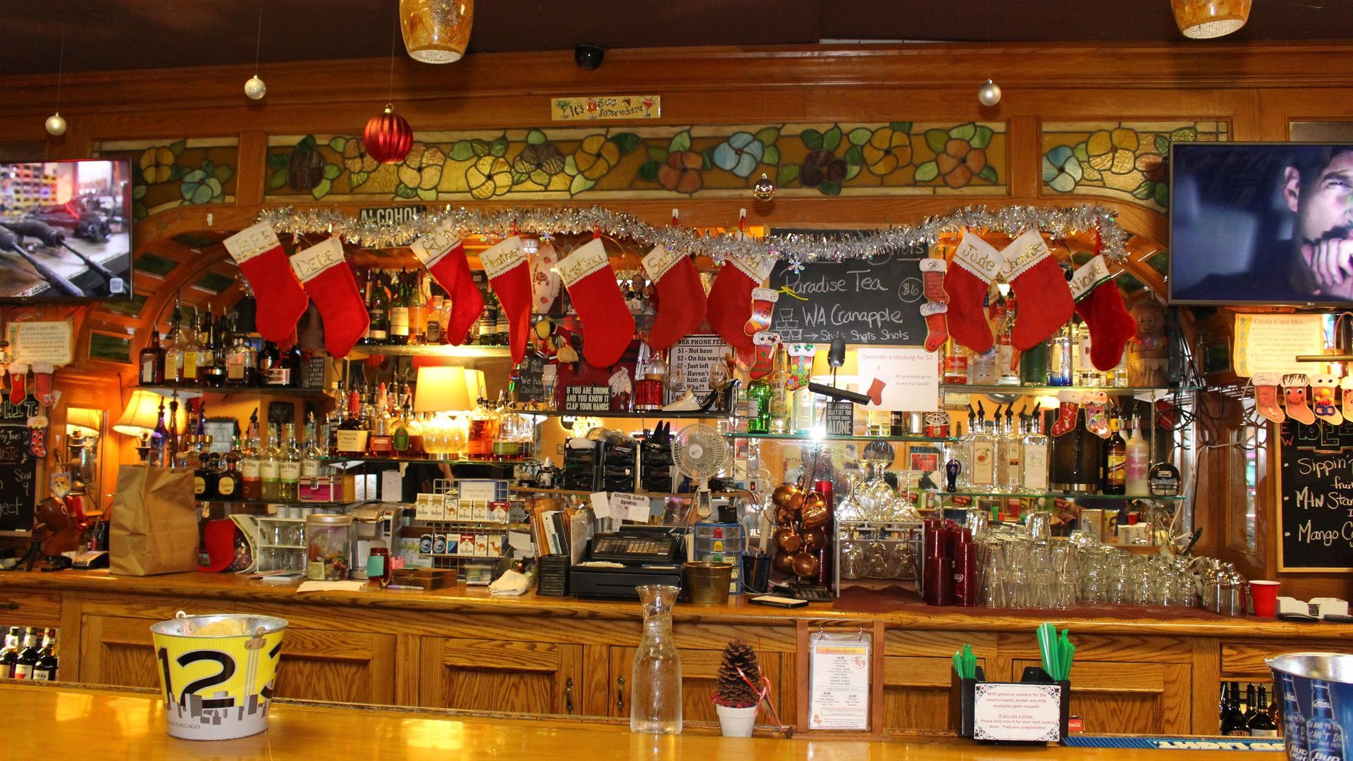 Bar decorated for Christmas with stockings, drinks, and televisions.