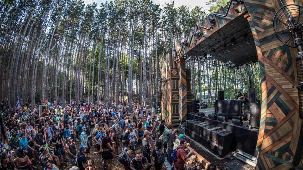 Crowd at outdoor music festival stage in a forest.