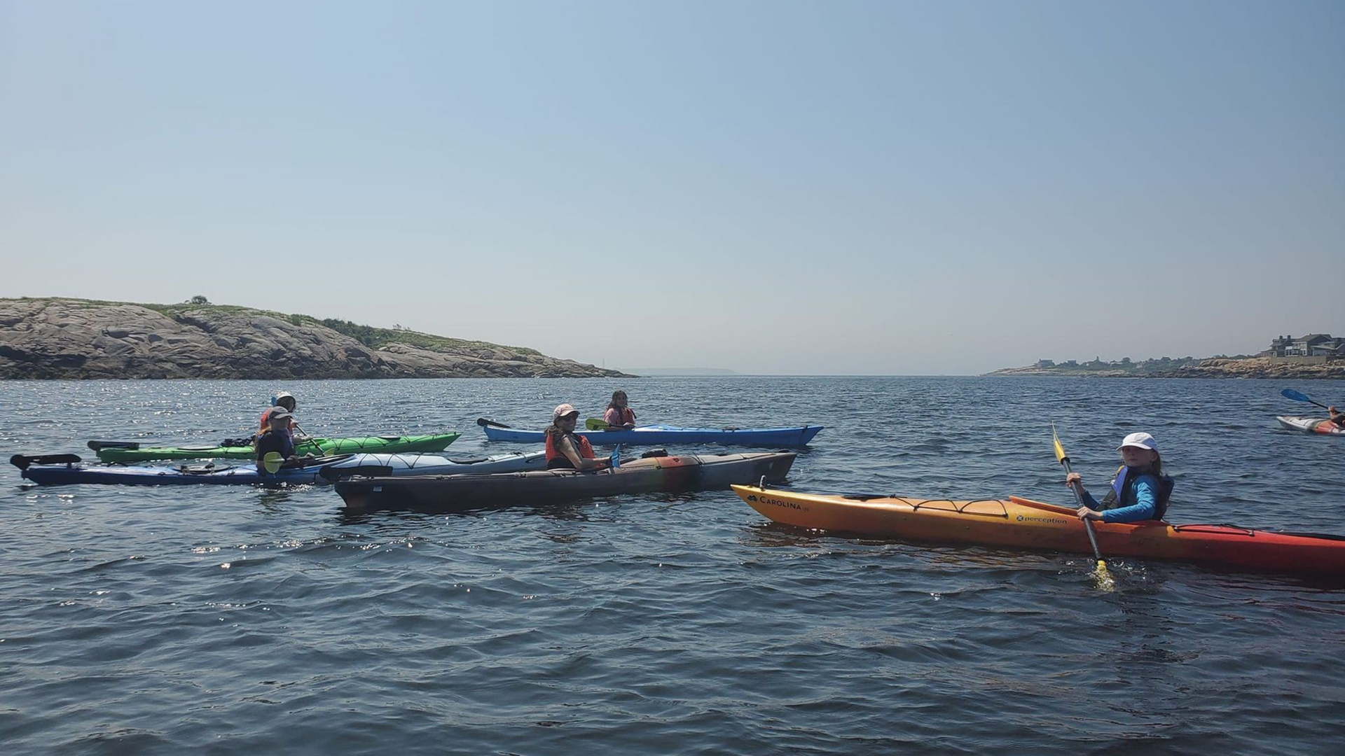 Kayakers on the open water near a rocky island on a sunny day.
