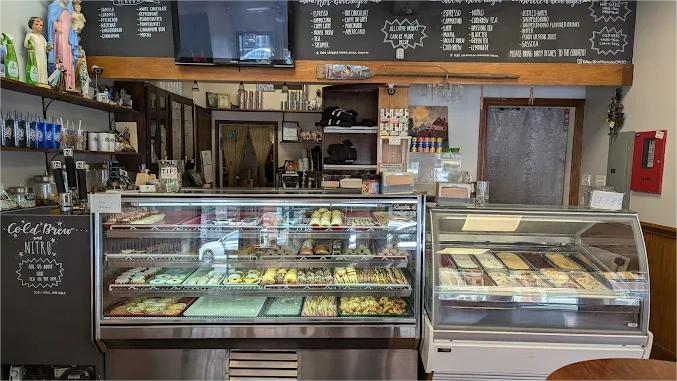 A cafe interior with glass display cases filled with pastries, blackboards with menu items, and a small TV.