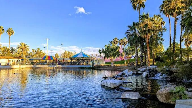 Scenic park with a pond, gazebo, palm trees, and clear blue sky.