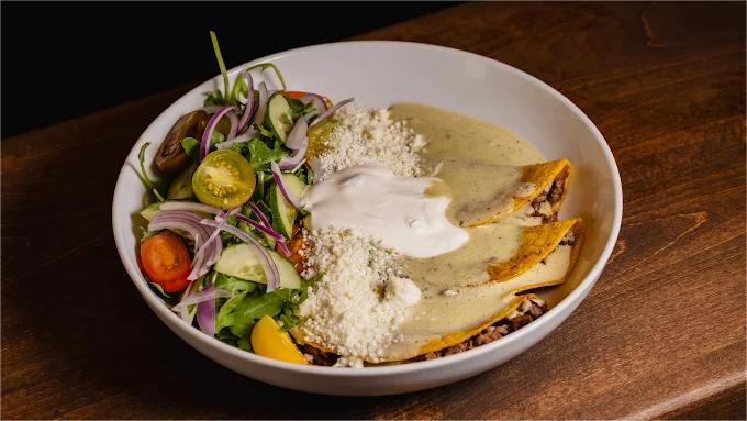 Bowl of enchiladas with salad, topped with cheese and sour cream.