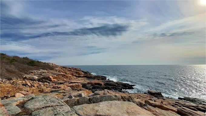 Rocky coastline with ocean waves under a partly cloudy sky.